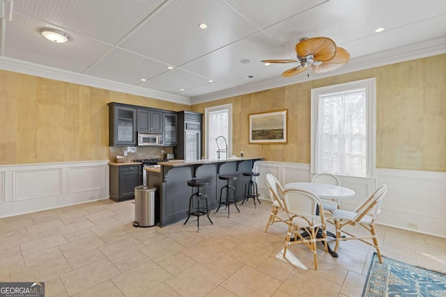 dining area with ornamental molding, a wainscoted wall, ceiling fan, and light tile patterned floors