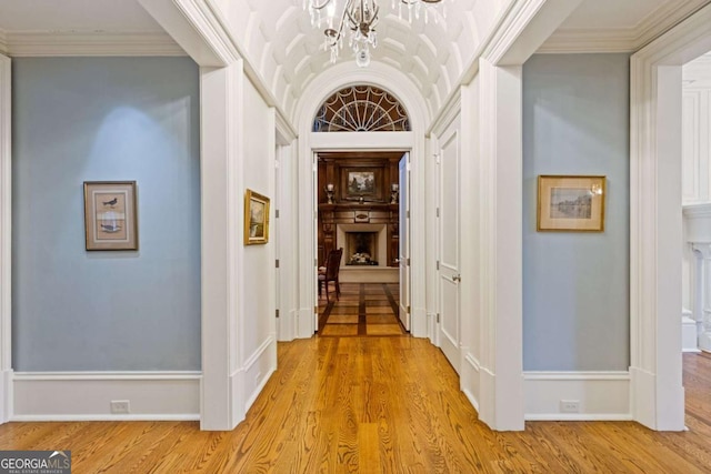 hallway featuring crown molding, a notable chandelier, light wood-style flooring, and baseboards