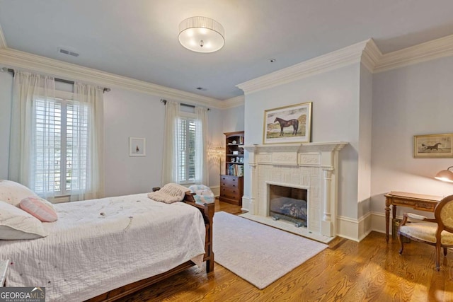 bedroom featuring a fireplace, visible vents, wood finished floors, and ornamental molding