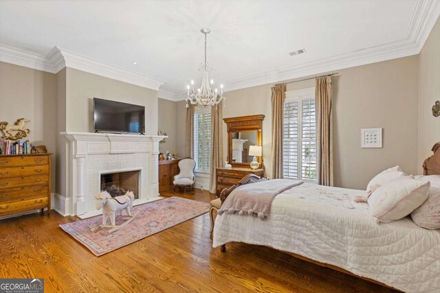 bedroom with a brick fireplace, visible vents, crown molding, and wood finished floors