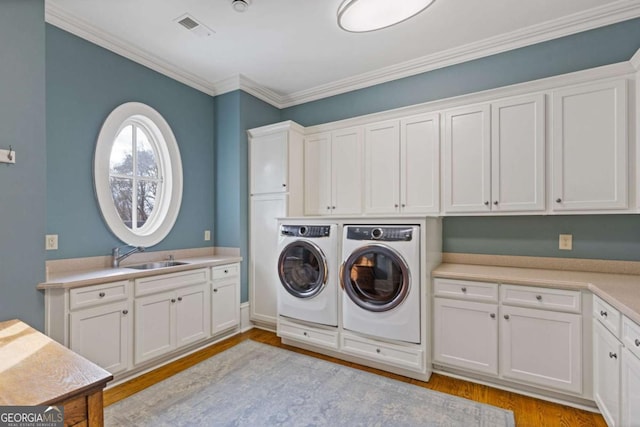 clothes washing area featuring light wood-style flooring, a sink, visible vents, washer and dryer, and cabinet space