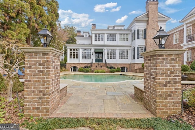 rear view of property featuring a patio area, a chimney, and an outdoor pool