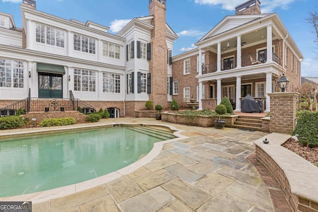 back of house featuring brick siding, a chimney, a patio area, a balcony, and an outdoor pool