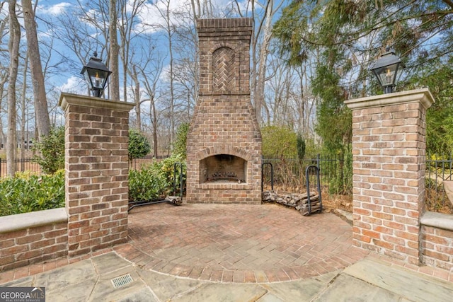 view of patio with an outdoor brick fireplace and fence