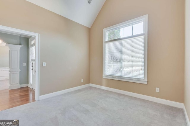 carpeted empty room with vaulted ceiling, baseboards, and ornate columns