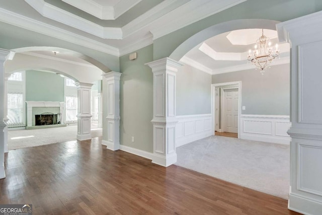 interior space with wood finished floors, a tray ceiling, crown molding, a fireplace, and a decorative wall