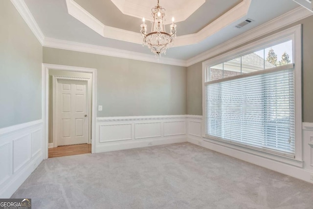 empty room featuring a notable chandelier, visible vents, ornamental molding, a tray ceiling, and carpet