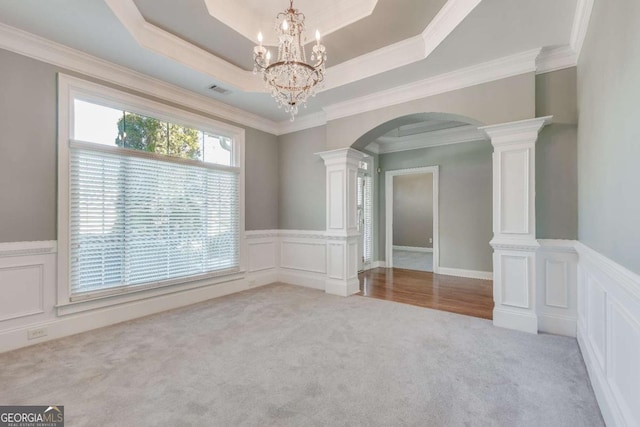 carpeted empty room featuring ornate columns, arched walkways, and a raised ceiling