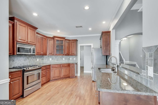 kitchen featuring arched walkways, appliances with stainless steel finishes, a sink, light stone countertops, and light wood-type flooring