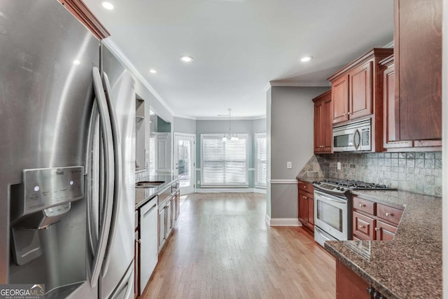 kitchen featuring stainless steel appliances, light wood-style flooring, decorative backsplash, ornamental molding, and dark stone countertops