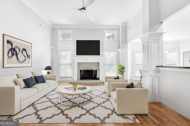 living room featuring ceiling fan, ornamental molding, a fireplace, and wood finished floors