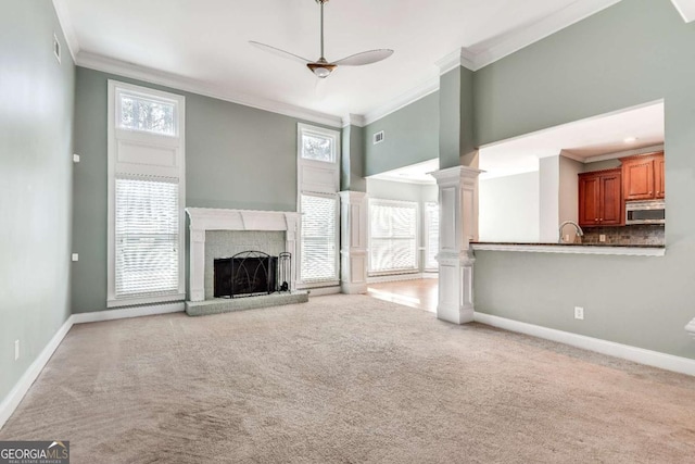 unfurnished living room featuring a fireplace with raised hearth, ornamental molding, a healthy amount of sunlight, and ornate columns