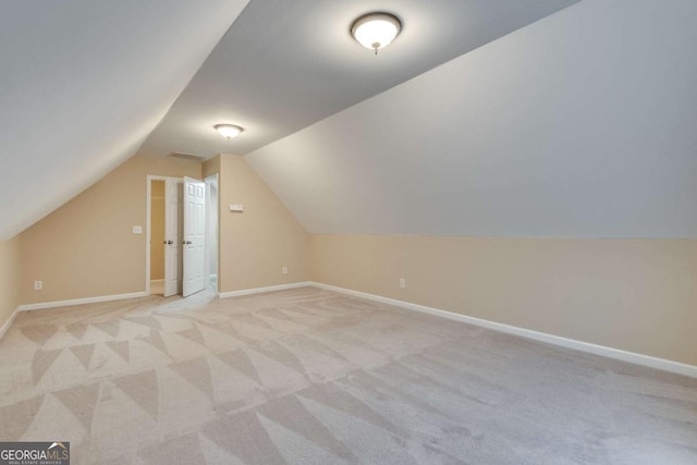 additional living space featuring light colored carpet, vaulted ceiling, and baseboards