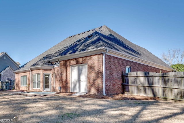 view of side of home featuring roof with shingles, fence, and brick siding