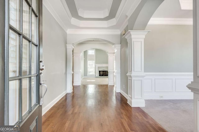 foyer entrance with decorative columns, arched walkways, a fireplace with raised hearth, ornamental molding, and a decorative wall