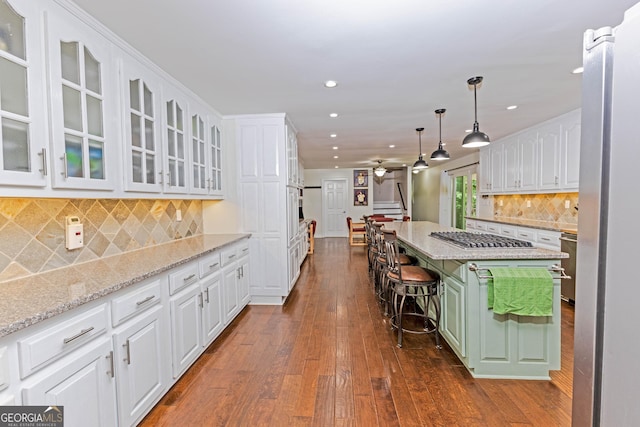 kitchen with a kitchen island, white cabinetry, appliances with stainless steel finishes, light stone countertops, and dark wood-style floors