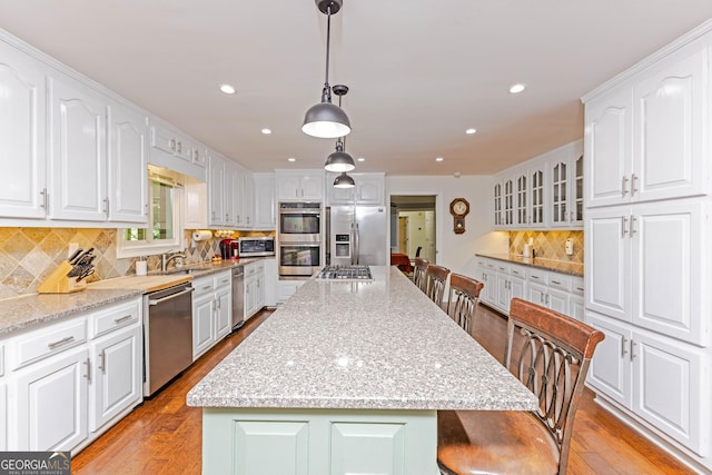 kitchen with a breakfast bar, stainless steel appliances, light wood-style flooring, white cabinetry, and a sink