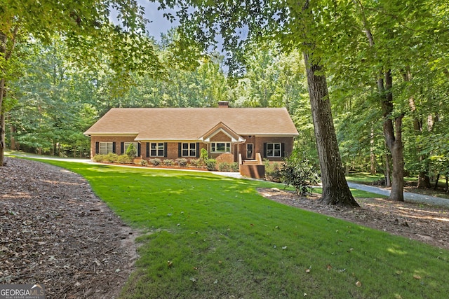 view of front of house with brick siding, a chimney, a front yard, and a wooded view