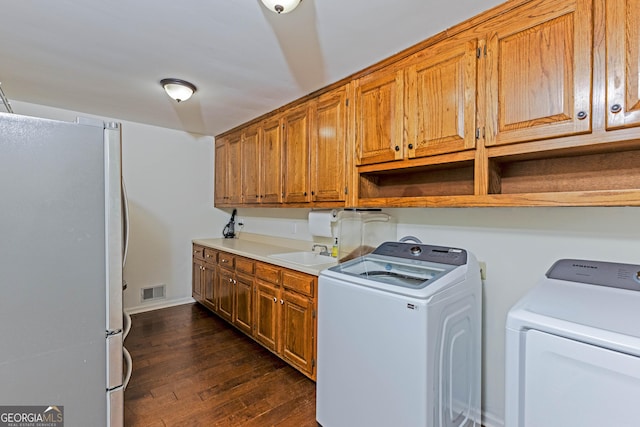 washroom with dark wood finished floors, washing machine and clothes dryer, visible vents, a sink, and baseboards