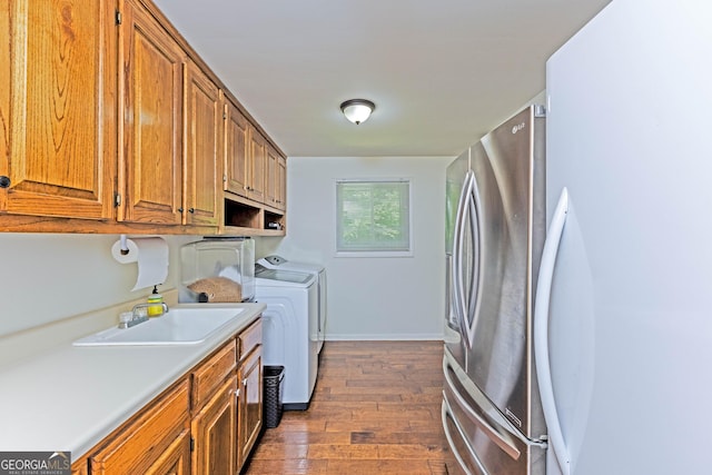 clothes washing area featuring dark wood-type flooring, a sink, baseboards, cabinet space, and washing machine and clothes dryer