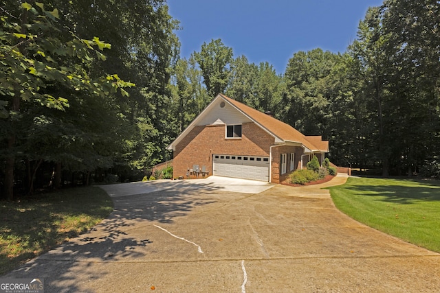 view of front facade featuring brick siding, an attached garage, a front yard, a wooded view, and driveway