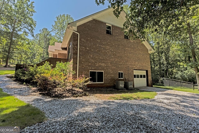 view of side of property with a garage, brick siding, driveway, and central AC unit