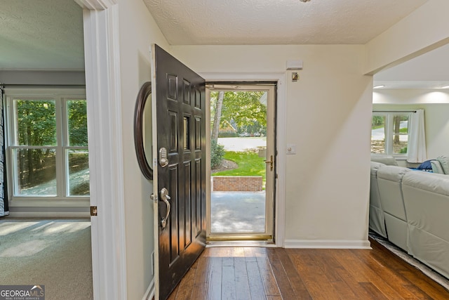 foyer featuring a water view, baseboards, dark wood finished floors, and a textured ceiling