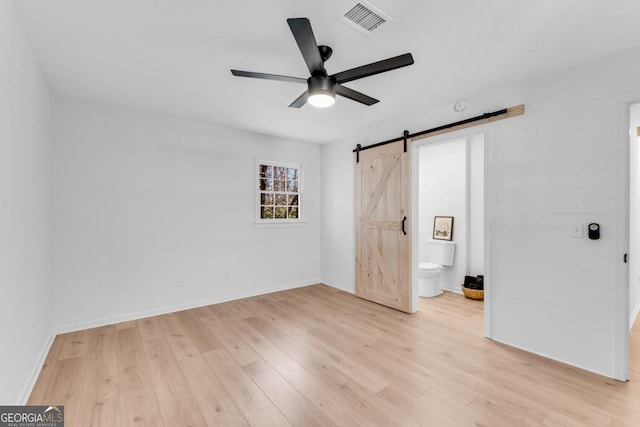 unfurnished bedroom featuring light wood finished floors, a barn door, visible vents, baseboards, and connected bathroom