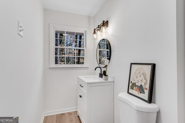 half bath featuring baseboards, vanity, toilet, and wood finished floors