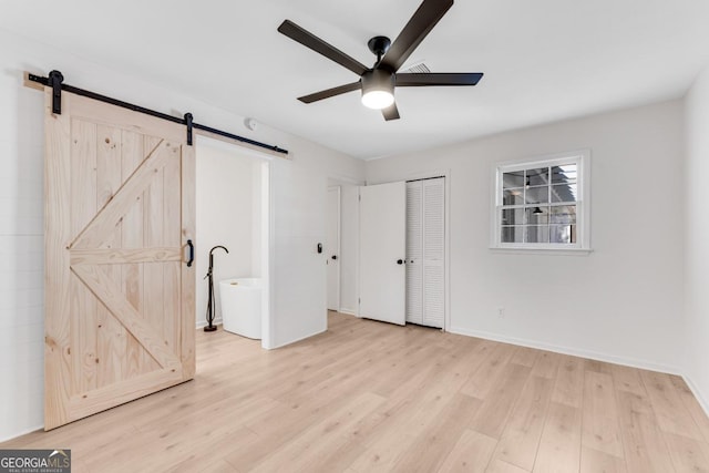 unfurnished bedroom featuring a closet, light wood-style flooring, baseboards, and a barn door