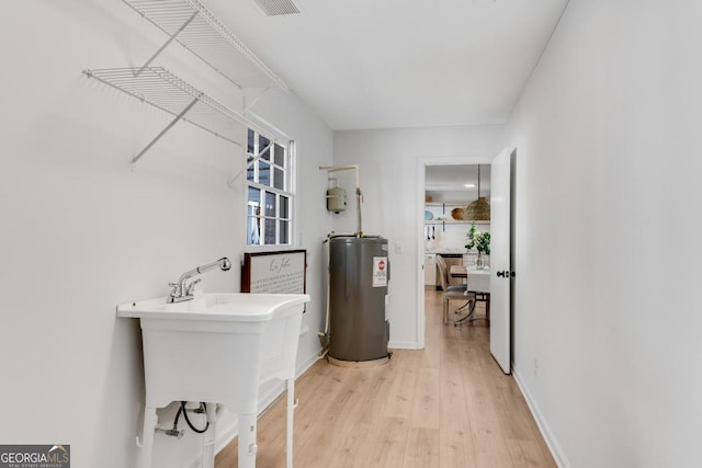 clothes washing area with baseboards, electric water heater, and light wood-style floors