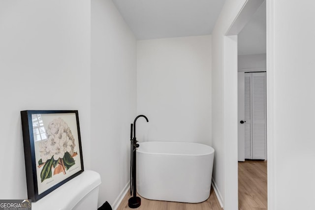 full bath with a freestanding tub, toilet, wood finished floors, baseboards, and a closet