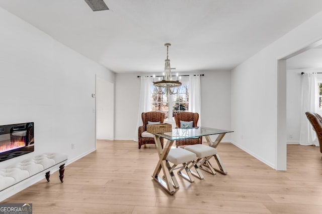 dining space featuring an inviting chandelier, a glass covered fireplace, visible vents, and light wood-style floors