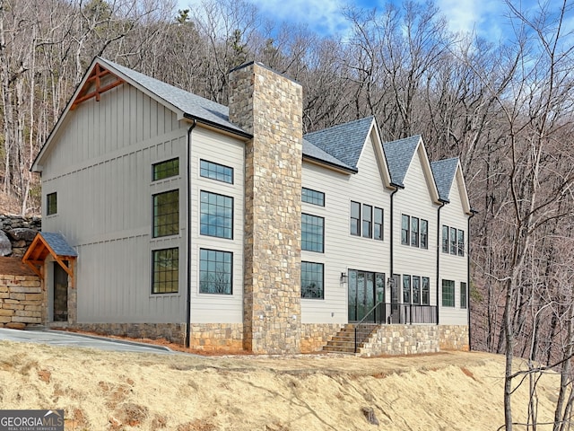 view of side of home with a shingled roof, a chimney, and board and batten siding