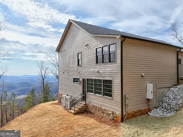 view of side of property with entry steps, a mountain view, and roof with shingles