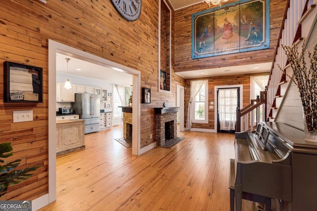 entryway featuring light wood finished floors, wooden walls, a high ceiling, stairs, and a fireplace