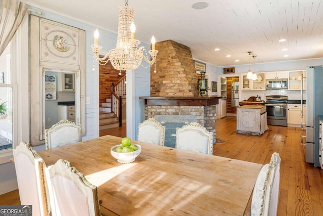 dining space with a fireplace, recessed lighting, light wood-style floors, a chandelier, and stairs