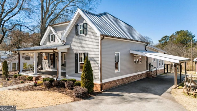 view of side of property with entry steps, metal roof, a porch, driveway, and a carport