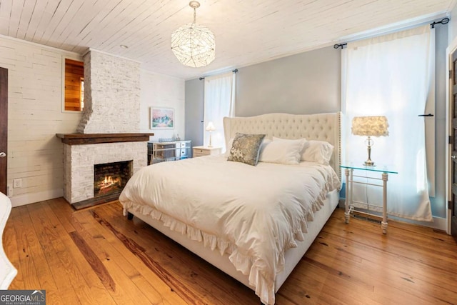 bedroom featuring ornamental molding, wood-type flooring, wooden ceiling, and a fireplace