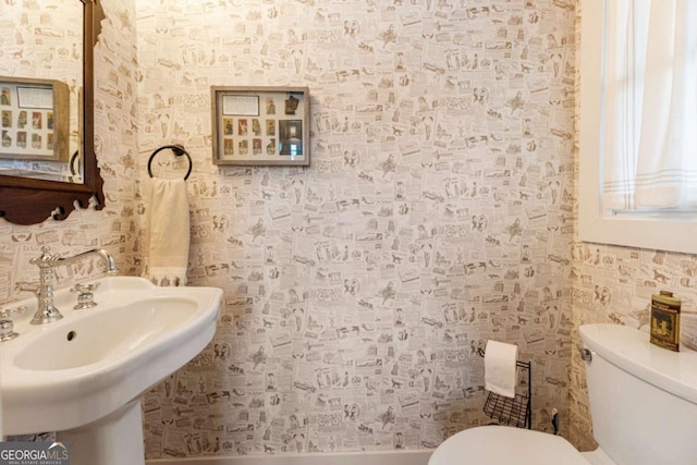 bathroom with a sink, toilet, and wallpapered walls