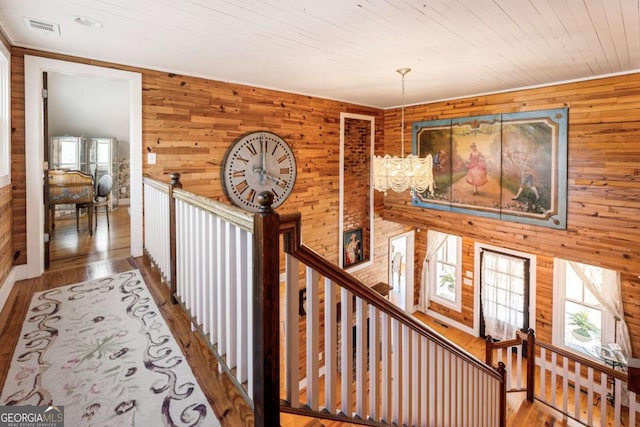 hallway featuring visible vents, wood walls, an upstairs landing, and wood finished floors