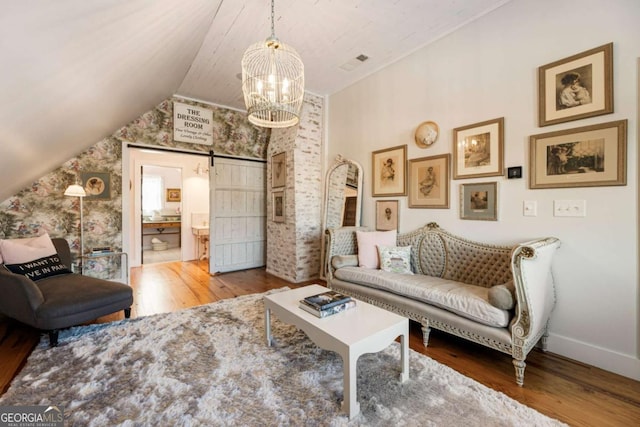 sitting room with a barn door, baseboards, wood finished floors, vaulted ceiling, and a notable chandelier