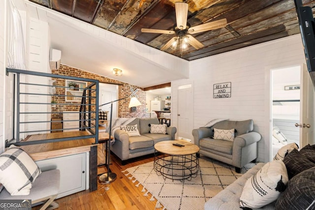 living room featuring a ceiling fan, brick wall, wood finished floors, a wall mounted air conditioner, and vaulted ceiling