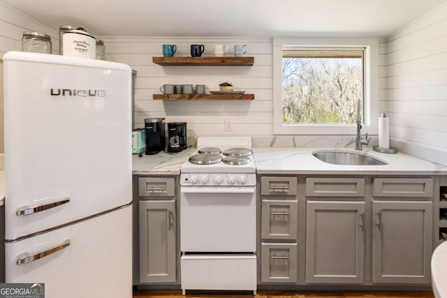 kitchen featuring white appliances, light stone countertops, gray cabinets, open shelves, and a sink