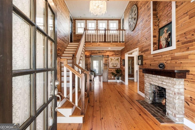 entryway featuring a barn door, a notable chandelier, stairway, a brick fireplace, and hardwood / wood-style floors