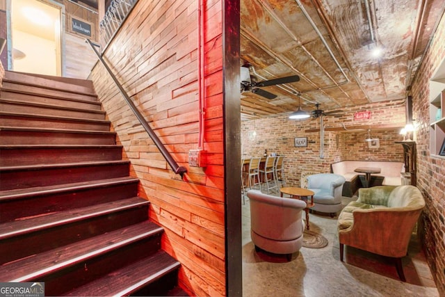 staircase featuring brick wall, ceiling fan, and concrete flooring