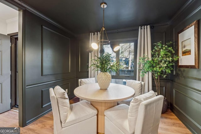 dining room with light wood-style floors, ornamental molding, a decorative wall, and a chandelier