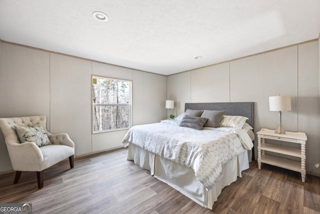 bedroom featuring a decorative wall, a textured ceiling, and wood finished floors