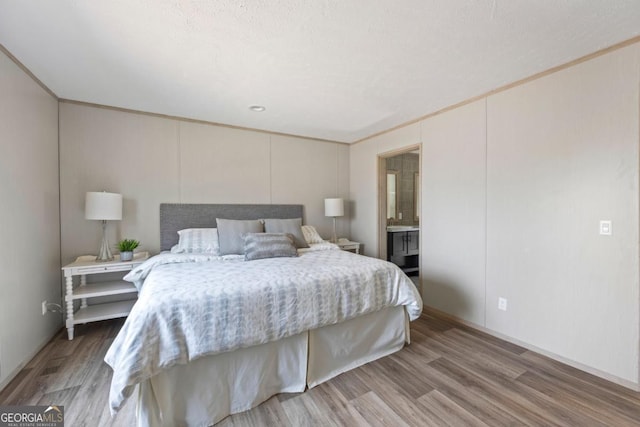 bedroom with ornamental molding, connected bathroom, a decorative wall, and wood finished floors