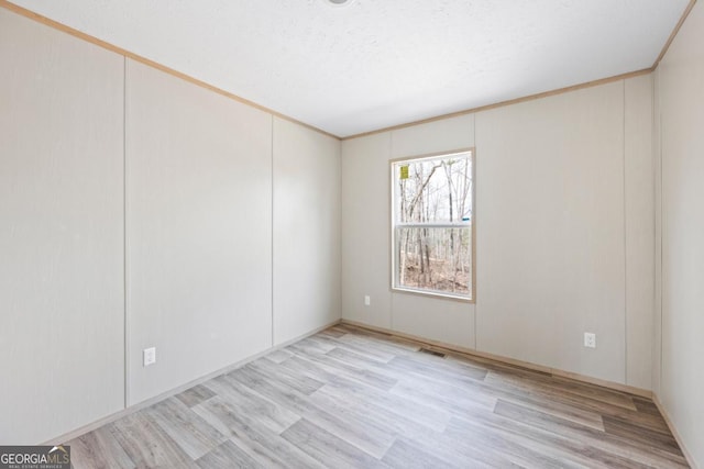 spare room featuring a textured ceiling, light wood-style flooring, ornamental molding, and visible vents